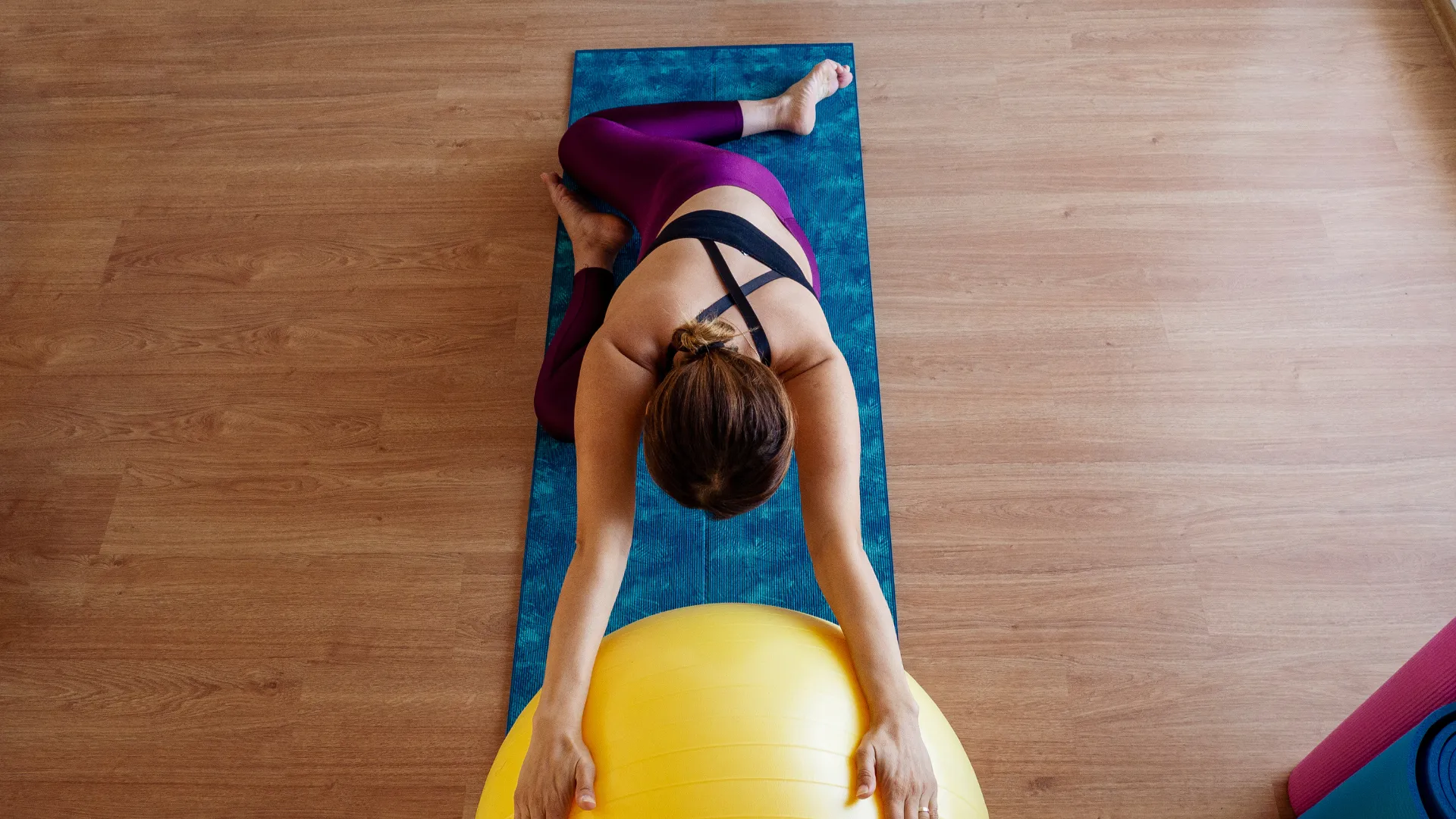 Donna esegue uno stretching con la fitball su un tappetino, vista dall'alto